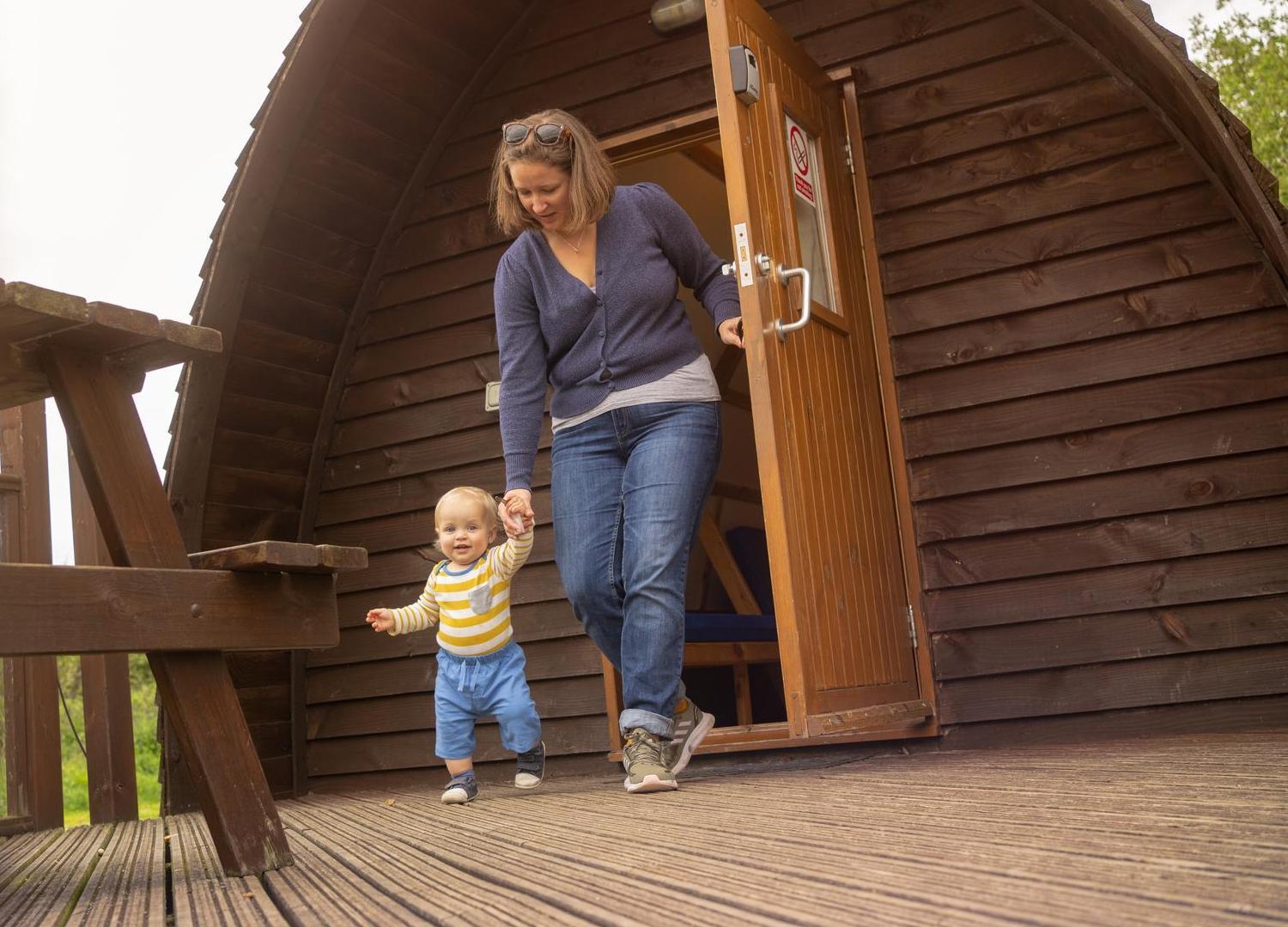 Lady with young child walking out of the door of a wooden Big Chief Wigwam at Lee Valley Caravan Park