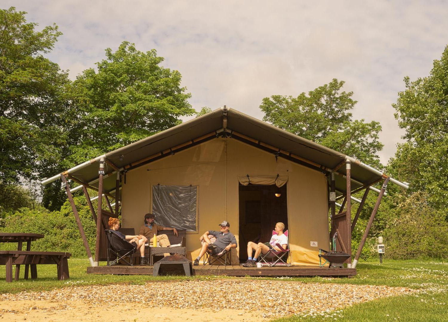 Large beige pre-ptiched safari tent at Lee Valley Caravan Park with people sat outside on decked area